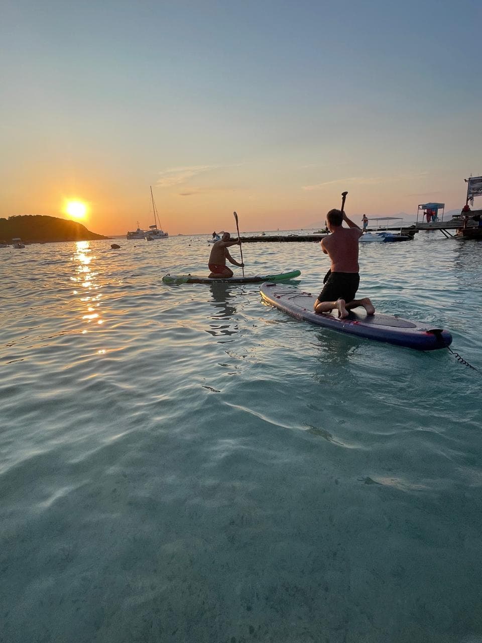 A serene side profile of a paddleboarder creating colorful sunset reflections on the calm Ionian Sea waters near Albania